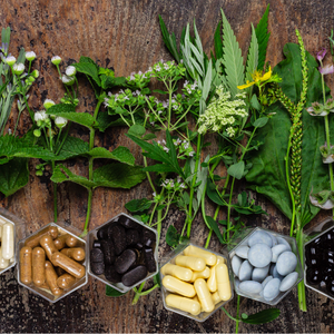 Various fresh herbs and multiple types of natural supplement capsules displayed on a rustic wooden background, symbolizing holistic health remedies.